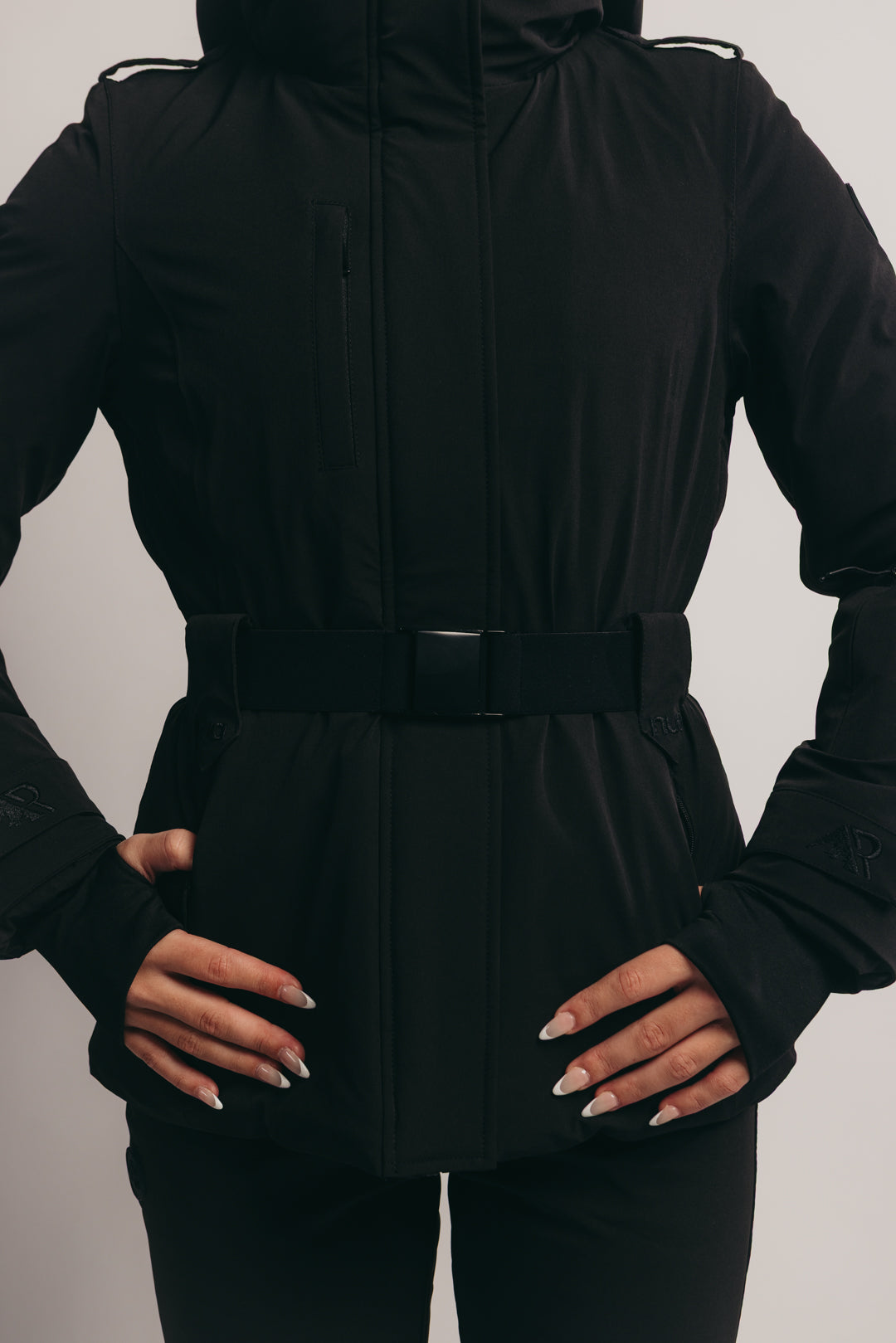 Person wearing a black ski jacket with a belt on a plain background