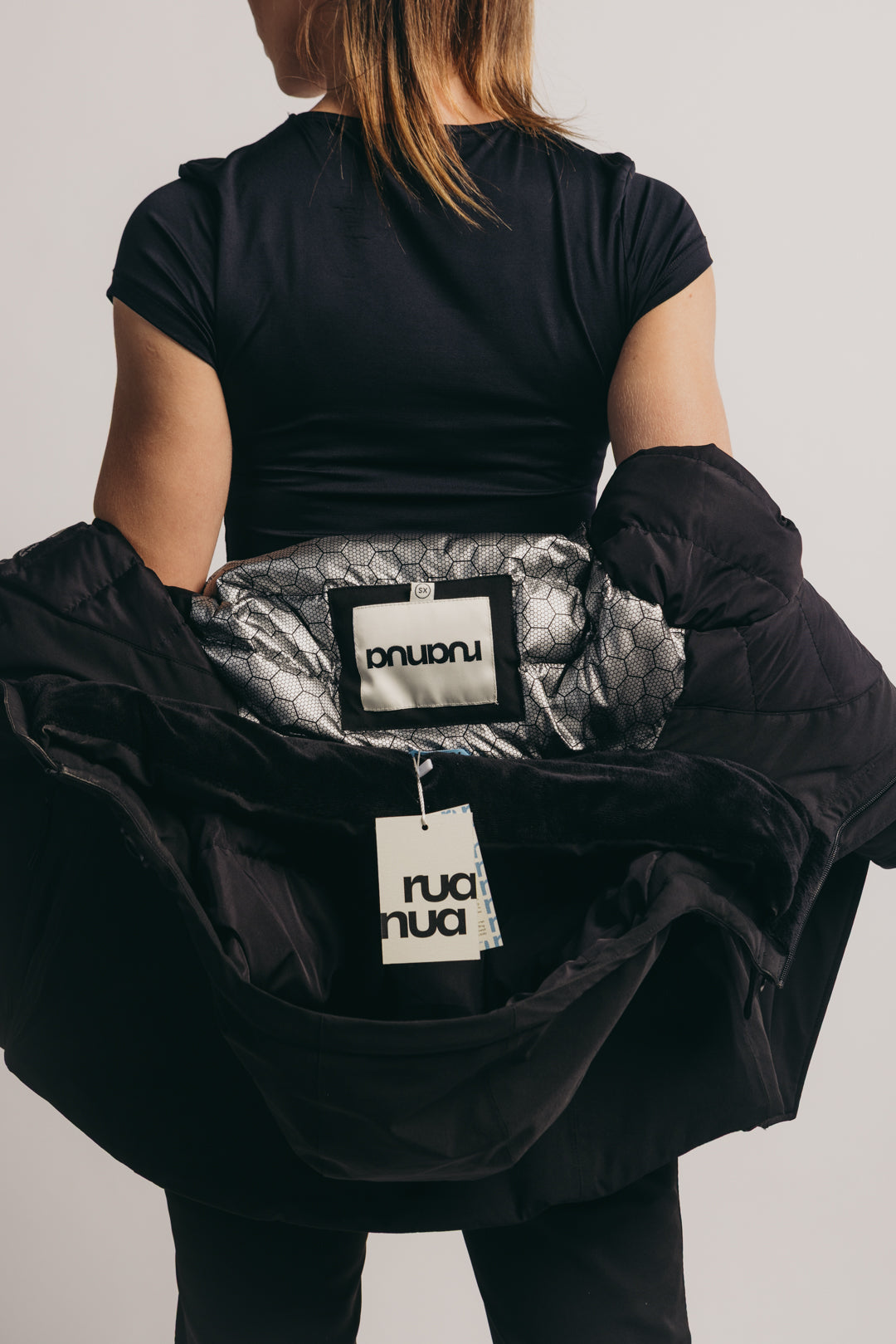 Person holding a black jacket with a brand tag on a plain background