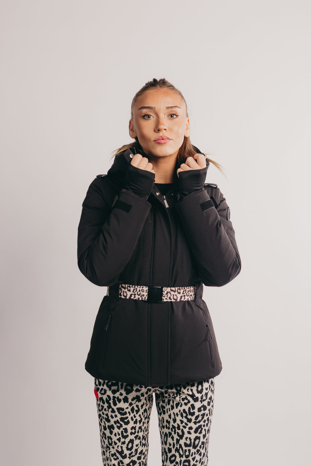 Person wearing a black puffer jacket with a leopard print belt and pants on a light gray background